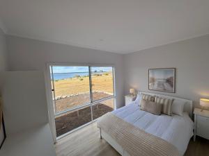 a white bedroom with a bed and a large window at Pelican Lagoon Retreat in Pelican Lagoon