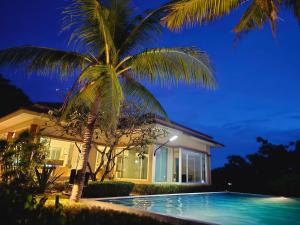 a palm tree in front of a house with a swimming pool at เดอรำพึง2 De ramphueng2 in Ban Chak Phai