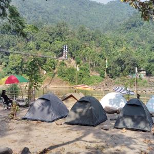eine Ansammlung von Zelten im Dreck mit einem Berg in der Unterkunft Tribe Riverbank Campsite in Dawki