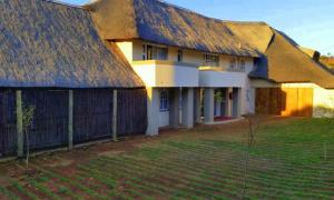 a large building with a thatched roof and a yard at Waterfall Guesthouse in Rustenburg