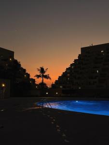 an empty swimming pool at sunset with a palm tree at Bab Al Bahr 2 BR Apartment in Ras al Khaimah