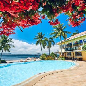 Una piscina tipo resort con palmeras y el océano. en Club Balai Isabel - Audrey-Adam Staycation Balai, en Sampong