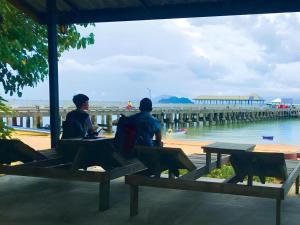 two people sitting on benches in front of a pier at Chomjan Hostel in Ko Phayam