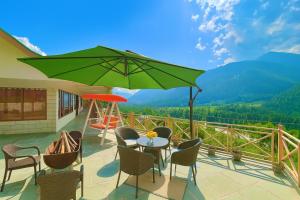 eine Terrasse mit Tisch, Stühlen und einem grünen Sonnenschirm in der Unterkunft Hotel Valley View with natural hot spring water Vashisht, Manali in Manali