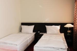 two beds in a room with white sheets and a lamp at Aariana Hotel in Offenbach