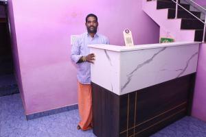 Arun Auro Residency في Kuilapayam: رجل يقف خلف المنضدة في غرفة أرجوانية