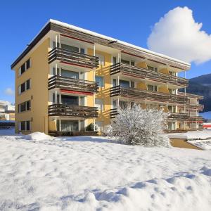 ein gelbes Apartmenthaus im Schnee in der Unterkunft Gemütliche Studios in Davos - Bergblick & zentrale Lage in Davos