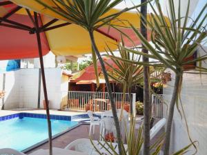 a pool with tables and umbrellas next to a pool at Pousada Maresias Guriri in Guriri