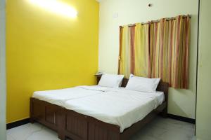 a bedroom with a bed with white sheets and a yellow wall at Laxmi Palaze in Tallākulam