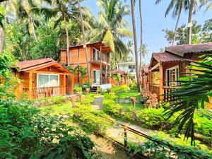 a resort with wooden cottages and palm trees at Tranquill riverview resort by trideus-Saipem, Candolim in Candolim
