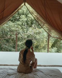 a woman sitting on a bed looking out a window at Autentik Penida "Glamping" - Adults only in Nusa Penida