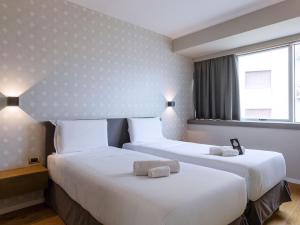 two beds in a hotel room next to a window at B&B HOTEL Trapani Crystal in Trapani