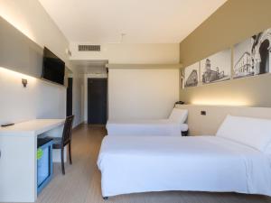 una habitación de hotel con dos camas y un escritorio en B&B Hotel Ferrara, en Ferrara