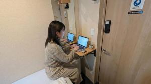 a woman sitting at a desk with a laptop computer at Sho inn MINIMAL HOTEL 小樽駅から無料送迎あり in Otaru