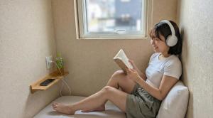 a woman wearing headphones sitting on a chair reading a book at Sho inn MINIMAL HOTEL 小樽駅から無料送迎あり in Otaru
