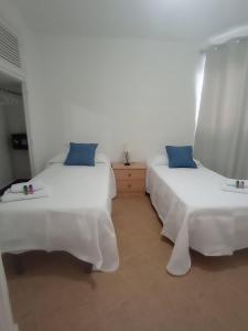 deux lits dans une chambre avec des murs blancs et des oreillers bleus dans l'établissement Apartamento Illa Blanca, à Es Pujols
