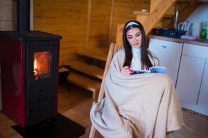 a woman sitting in a chair under a blanket in front of a fire at Vikendica i odmaraliste JuliE, Sarajevo-Jahorina in Tvrdimići +50 photos