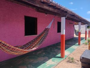 un bâtiment rose avec un hamac à l'extérieur dans l'établissement Hostel Mamitchesca - Redes e Barracas, à Aracati