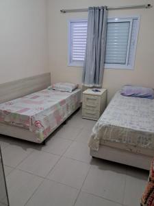 two beds in a room with two windows at Apto Pe na areia # Piscina e Churrasqueira in Mongaguá