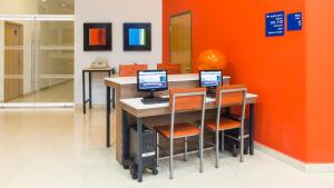 an office with three computers on a desk with an orange wall at Holiday Inn Express Manzanillo by IHG in Manzanillo