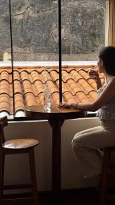 a woman sitting at a table looking out a window at Hotel Boutique MIRANDO AL SOL in Ollantaytambo