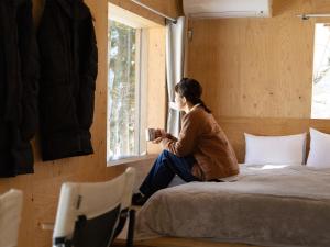 a woman sitting on a bed looking out the window at Snow Peak LAND STATION HAKUBA in Hakuba