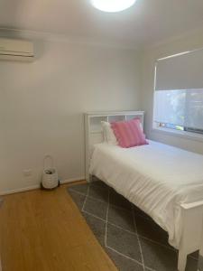 a bedroom with a white bed with a pink pillow at Coastal play and stay - walk to beach and park in Toowoon Bay