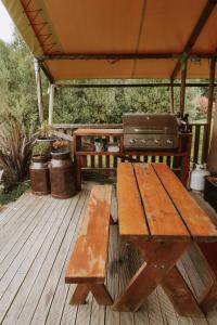 Una mesa de picnic de madera en una terraza con parrilla. en Raglan Rural Retreats - Rimu Tent, en Raglan