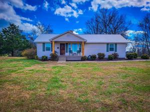 een wit huis met blauwe ramen op een tuin bij Cozy 3BR Cottage with Firepit Sleeps 10 Close to Lake Fun in Scottsboro