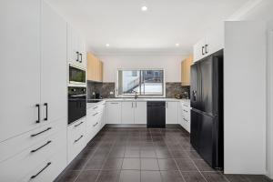 a kitchen with white cabinets and a black refrigerator at Galoola Hidden Gem - 2,97 Galoola Drive, Rooftop outdoor area with spectacular views, Wi-Fi and air conditioning. in Nelson Bay