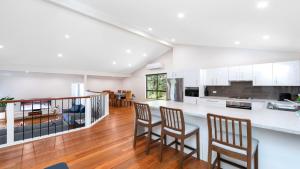 a kitchen with white cabinets and bar stools at 'Treetops On The Bay - Water Views' by HolidayCo in Hardys Bay