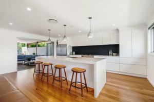 a kitchen with a white counter and bar stools at Forresters Lodge by Coast Hosting in Wamberal North