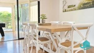 a dining room with a wooden table and white chairs at Village Bay Lake house family Lake House with Spa in Marks Point