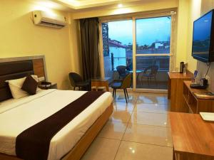 a hotel room with a bed and a television and a balcony at MLS Prime Inn - Near Dehradun Railway Station in Dehradun