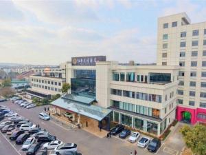 ein großes Gebäude mit auf einem Parkplatz abgestellten Autos in der Unterkunft Zhangjiagang Jiangnan Garden Hotel in Xiwujieqiao