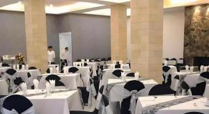 WanasariSelabintana Conference Resort的宴会厅里摆着白色的桌椅，还有两个人