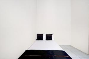 Una cama blanca con dos almohadas negras en una habitación. en OYO 95041 Griya Indah Homestay, en Djetak