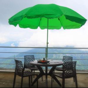 a table with chairs and a green umbrella on a balcony at Aman magic resort in Takdāh