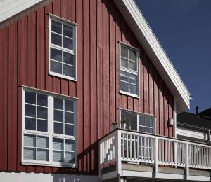 特希尔Schwalbennest Greetsiel für bis zu 6 Personen mit Kaminofen, Whirlpool und Sauna - Haustiere herzlich willkommen, nah am Hafen的红色的房子设有白色窗户和阳台