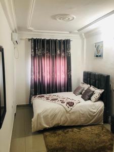 una camera da letto con un letto e una finestra con tende di MADO Appartement a Bonamoussadi