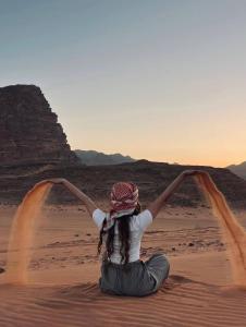 a girl sitting in the desert with her arms in the air at Spirit of the Badia camp in Disah
