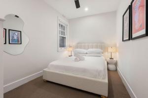 Un dormitorio blanco con una cama blanca y un espejo. en Fresh & Comfy 3BR Near The Rocks, en Sídney 14 fotos más
