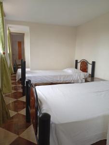 zwei Betten in einem Zimmer mit weißen Laken in der Unterkunft Mini Apartamento Rural Fusagasuga Finca los Pinos in Fusagasuga