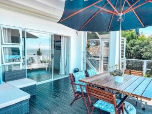 a porch with a wooden table and chairs and an umbrella at Harker Street Sea Facing Studio in Plettenberg Bay