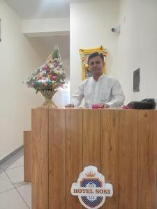 a man standing behind a wooden podium with a vase at Hotel Soni Indore in Indore