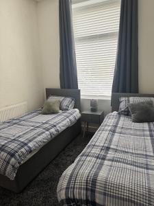 a bedroom with two beds and a window with blue curtains at Holgate Cottage in Great Harwood