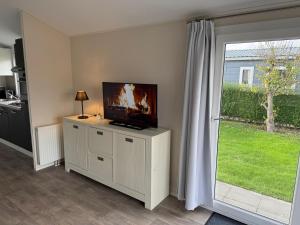 a living room with a television on a dresser with a window at Ferien-Chalet Oostkapelle in Oostkapelle