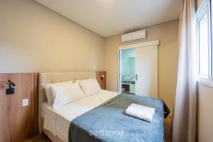 a bedroom with a bed with a blue blanket and a window at Apto c/ Churrasqueira a 500m da Praia TDF0302 in Itapema