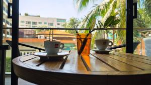 Beautiful Pool View Studio in Kata في شاطئ كاتا: طاولة خشبية مع كوبين من القهوة ومزهرية
