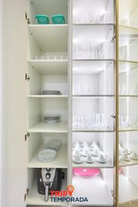 a white pantry with glasses and dishes on shelves at Apartamento espaçoso com ar condicionado e Wi-fi, a 100 metros da praia - Edifício Estoril in Ubatuba